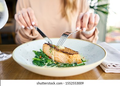 Salmon steak fillet with grainy mustard and spinach. Lunch in a restaurant, a woman eats delicious and healthy food. Restaurant menu, a series of photos of different dishes