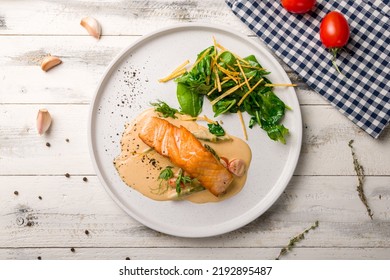 Salmon steak on the grill with spinach on white plate on white wooden table top view
