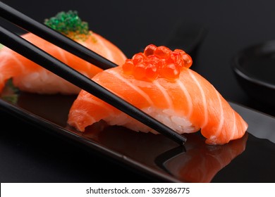 Salmon sushi nigiri in chopsticks over black background - Powered by Shutterstock