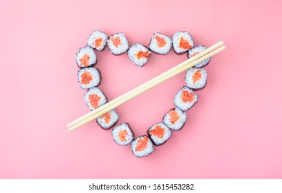 Salmon sushi rolls laid out in the shape of a heart on a pink background. The concept of Japanese cuisine for Valentine's Day, greeting card, banner. Copy space
