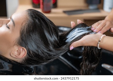 In a salon setting, a stylist delicately applies conditioner to the woman's hair, enhancing its softness and shine - Powered by Shutterstock