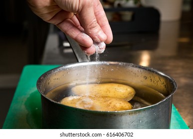 Salt Being Dropped Into A Pan Of Hot Water Containing Potatoes