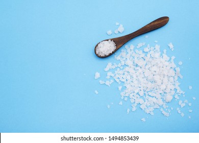 Salt grain in wooden spoon top view on blue background , flat lay.