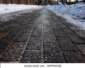 Salt Grains On Icy Sidewalk Surface In The Winter. Applying Salt To Keep Roads Clear And People Safe In Winter Weather From Ice Or Snow, Closeup View.