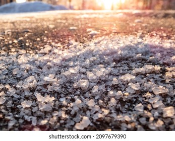 Salt grains on icy sidewalk surface in the winter. Applying salt to keep road clear and people safe in winter weather from ice or snow. Macro view of salt grains in sunlight in winter