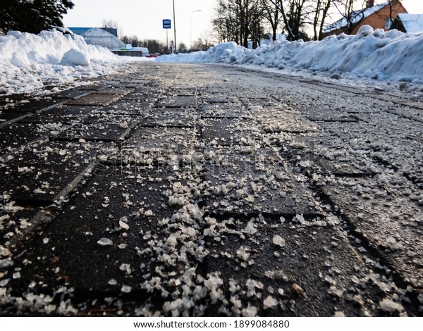 Salt grains on icy sidewalk surface in the\
winter. Applying salt to keep roads clear and people safe in winter\
weather from ice or snow, closeup\
view.