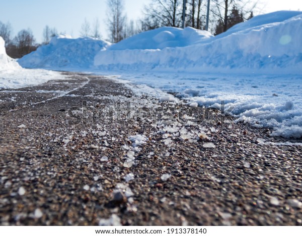 Salt grains on icy sidewalk surface in the\
winter. Applying salt to keep roads clear and people safe in winter\
weather from ice or snow, closeup\
view
