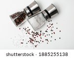 Salt and pepper grinders. Dried whole seed of black pepper and white coarse sea salt isolated on a white background seen from above. 