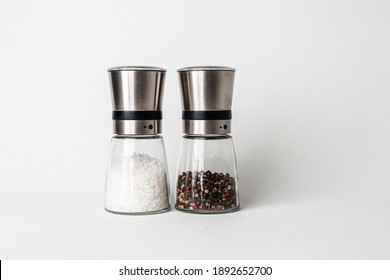 Salt And Pepper Grinders. Dried Whole Seed Of Black Pepper And White Coarse Sea Salt Isolated On A White Background Seen From Above. 