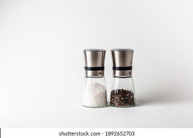 Salt And Pepper Grinders. Dried Whole Seed Of Black Pepper And White Coarse Sea Salt Isolated On A White Background Seen From Above. 