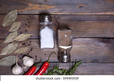 Salt And Pepper Shaker With Bay Leaf And Red Chili Pepper, White Garlic On Background Of Wood, Top View Of The Workspace.