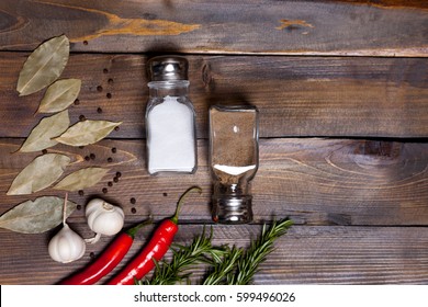 Salt And Pepper Shaker With Bay Leaf And Red Chili Pepper, White Garlic On Background Of Wood, Top View Of The Workspace.