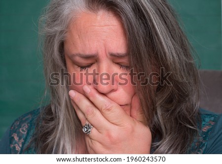 salt and peppered grey haired woman grieving sadness with hand over mouth eyes closed about to cry
