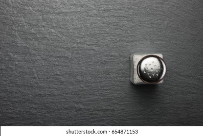 Salt Shaker With White Salt On Black Stone Background, Top View