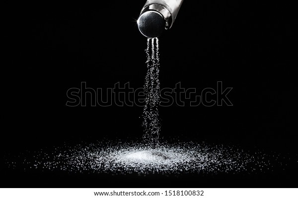 Salt spills out of the salt\
shaker in thin streams on a black background.Concept\
salting/