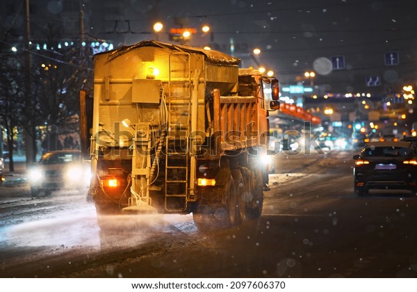 Salt spreading on road by municipal cleaning\
service. Snow plow service truck removing snow and spreading salt\
on snowy city road during blizzard, night work road maintenance.\
Snow removing service