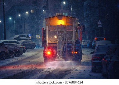 Salt spreading. Snow plow service truck removing snow and spreading salt on snowy city road during blizzard, night work road maintenance. Truck spreading de-icing salt on snowy and icy asphalt road