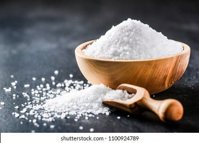 Salt in wooden scoop on dark stone table.