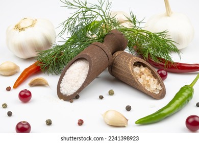 Salt in wooden spoons, spices, dill, hot pepper and garlic isolated on a white background.