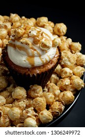 Salted Caramel Cupcake Sitting On Cake Stand With Caramel Popcorn - Dark Background