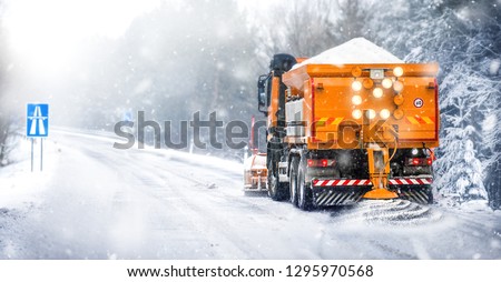 Salting highway maintenance. Snow plow truck on snowy road in action. Hard weather condition in winter. Gritter vehicle spreading deicing salt.