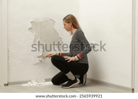 Saltpeter or mold on the wall problem. Woman is using a scraper to scrape and remove all loose paint and plaster that is in poor condition, until a firm surface is achieved.