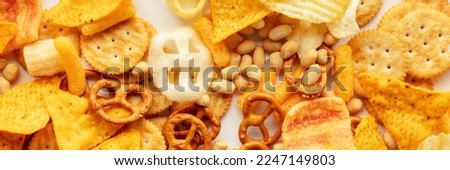 Salty snacks panorama. Party food on white banner. Potato and tortilla chips, crackers and other appetizers, overhead flat lay panoramic shot