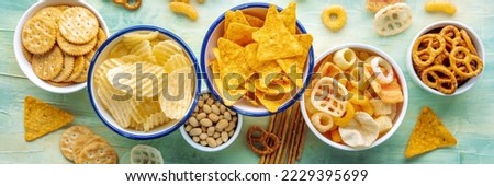 Salty snacks panorama. A table of assorted appetizers in bowls, overhead panoramic banner with a flat lay of party food on blue