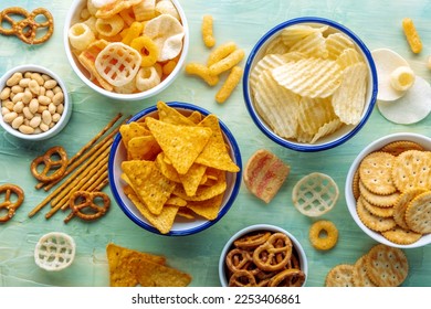 Salty snacks. Party food on a blue background. Potato and tortilla chips, crackers and other appetizers in bowls, overhead flat lay shot - Powered by Shutterstock