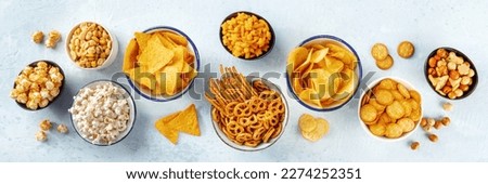 Salty snacks, party mix, overhead flat lay panorama. An assortment of appetizers. Potato and tortilla chips, crackers, popcorn etc panoramic banner