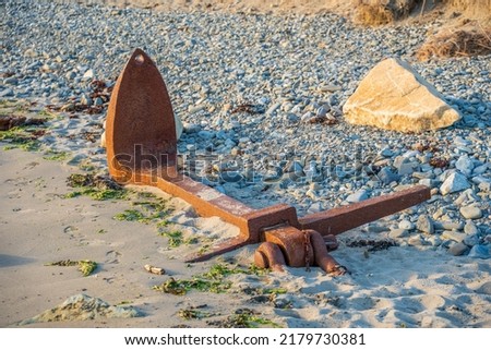 salvaged rusty shipwrecked boats anchor from the sea bed  partially buried in the sand on a rocky pebble beach