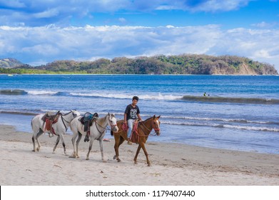 Samara, Costa Rica, June, 26, 2018: Teenager horseback Riding in the beach, white sand of Samara in a beautiful sunny day with blue sky and blue water in Costa Rica