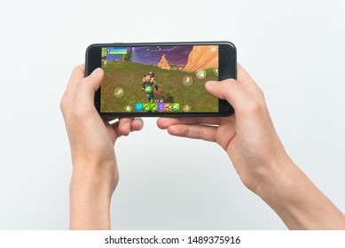Samara, Russia -07, 29, 2019: A young guy playing Fortnite game on Iphone 8 Plus. Teenage boy holding a phone in his hands with a game Fortnite battle royale on a white background.