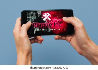 Samara, Russia -07, 29, 2019: A young guy playing Plague Inc: Evolved game on Iphone 8 Plus. Teenage boy holding a phone in his hands with a game Plague Inc on a blue background.