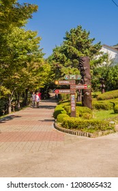 Samcheok, South Korea; September 25, 2018: Unidentified Asian Couple Walking On Brick Sidewalk As They Look At Phallic Statues In  Mountainside Park 