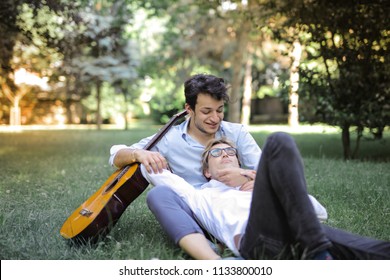 Same Sex Couple Relaxing In A Park With A Guitar