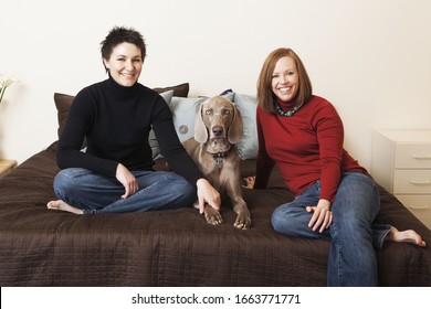 A Same Sex Couple, Two Women Posing With Their Weimeranar Pedigree Dog Between Them.