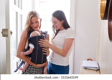 Same Sex Female Couple With Baby Daughter In Sling Opening Front Door Of Home