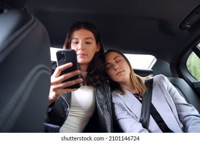 Same Sex Female Couple In Back Of Taxi Sleeping And Looking At Mobile Phone