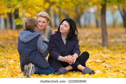 A Same Sex Female Couple Listening To Their Son Intently In An Autumn Park Setting.