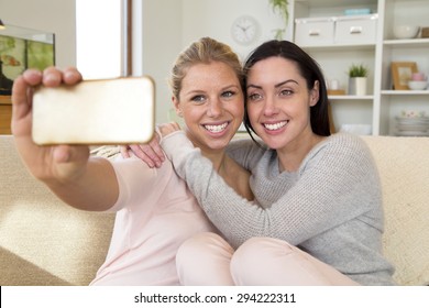 Same Sex Female Couple Taking A Selfie Using A Mobile Phone In Their Home