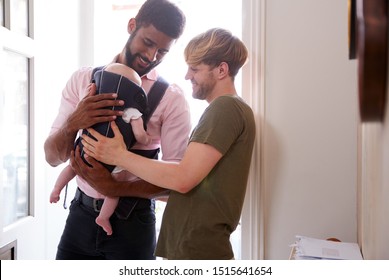 Same Sex Male Couple With Baby Daughter In Sling Opening Front Door Of Home