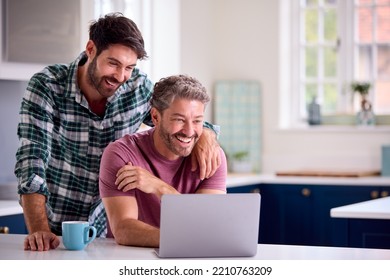 Same Sex Male Couple Using Laptop At Home To Check Finances Book Holiday Or Shop