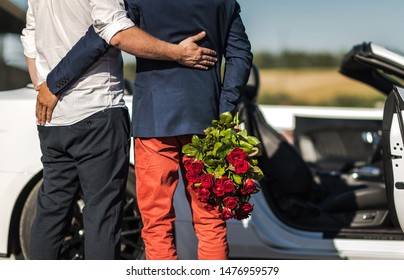 Same SexRelationship. Gay Couple In Front Of A Car. One Men With Bouquet Of Red Roses.