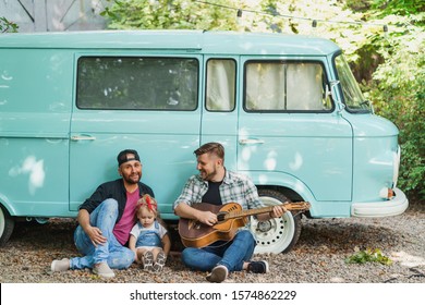 Same-sex Family With Kid Resting Near Their Car Van, Playing Guitar And Singing A Song. Family Harmony.