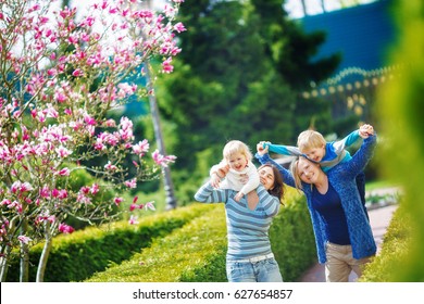 Samesex Lesbian Family With Two Children On A Walk In The Park. Children Have Fun Sitting On Their Mother's Neck