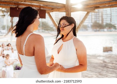 Same-sex Marriage Image Of Two Women On The Beach. Gay Girls Getting Married In A Beautiful Sunset On The Rocks Near The Beach. Real Wedding.