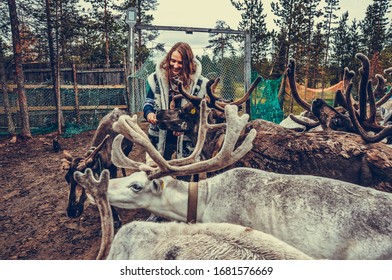 Sami Village, Sam-Syyt / Russia - August 6 2019: A Girl In Sami Clothes Stands Next To A Reindeer And Feeds Them