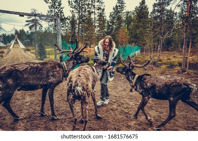 Sami Village, Sam-Syyt / Russia - August 6 2019: A Girl In Sami Clothes Stands Next To A Reindeer And Feeds Them