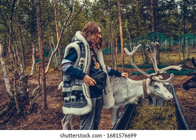 Sami Village, Sam-Syyt / Russia - August 6 2019: A Girl In Sami Clothes Stands Next To A Reindeer And Feeds Them